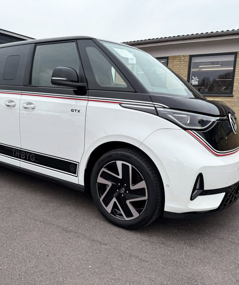 Denne VW ID. Buzz GTX har fået et markant og sporty udtryk med sort delindpakning af bilens øverste del kombineret med specialdesignet foliedekoration. De gennemgående striber i sort, hvid og rød følger bilens linjer fra front til bag og binder designet sammen, mens den sorte overdel giver bilen et mere eksklusivt og karakterfuldt udtryk. Opgaven omfattede: Delindpakning · Specialdesign · Foliedekoration